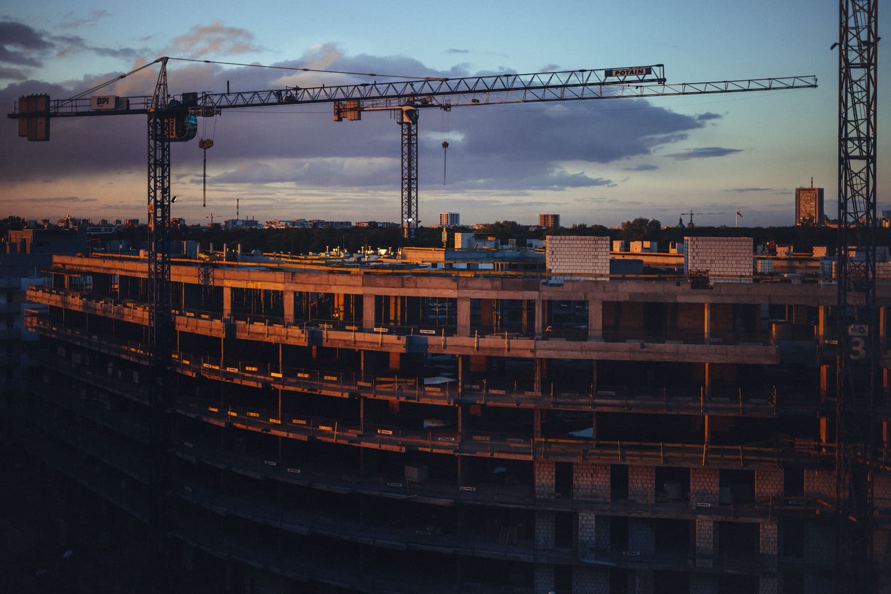 Tower cranes over a curved multi-storey concrete structure at dusk