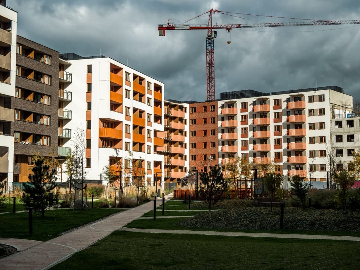 Completed apartment blocks with orange balconies around landscaped grounds, a tower crane behind